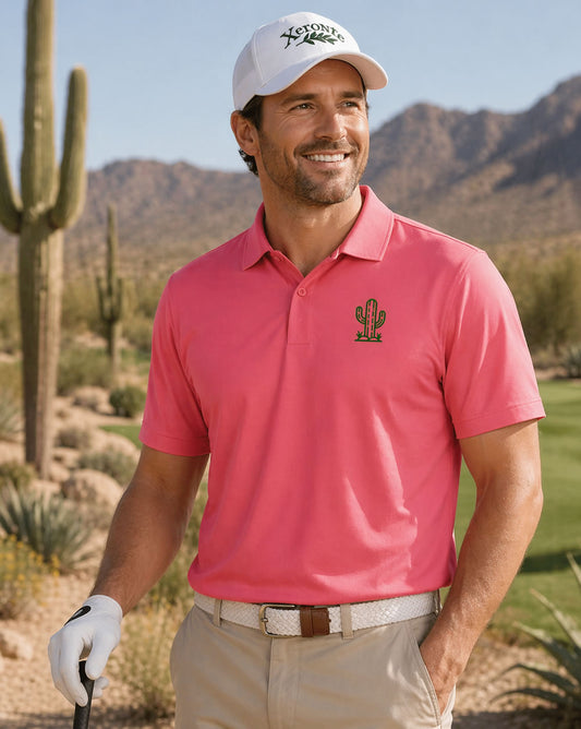 Man wearing a pink polo shirt with a cactus design, white cap, and golf glove in a desert setting.