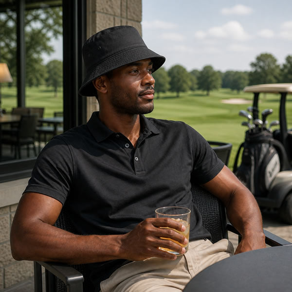Man in black shirt and hat holding a drink, sitting on a golf course