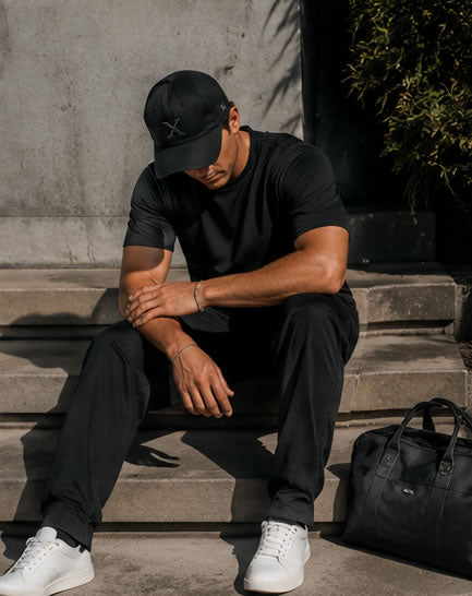 Man sitting on steps wearing a black outfit with a golf dad hat