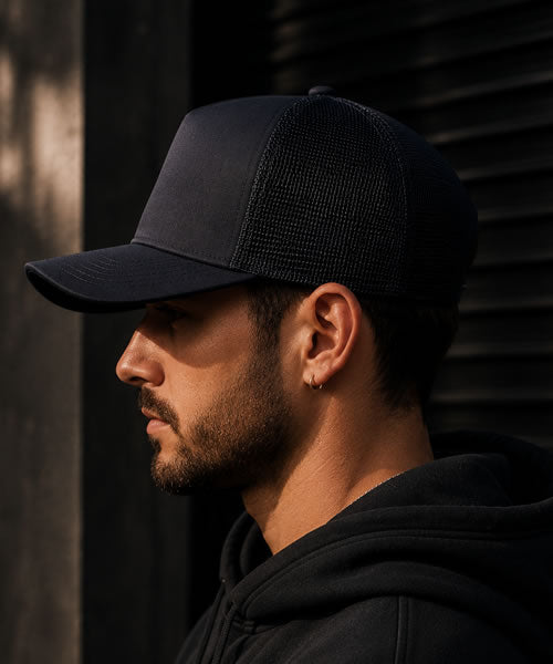 Man wearing a black trucker hat and hoodie against a dark background